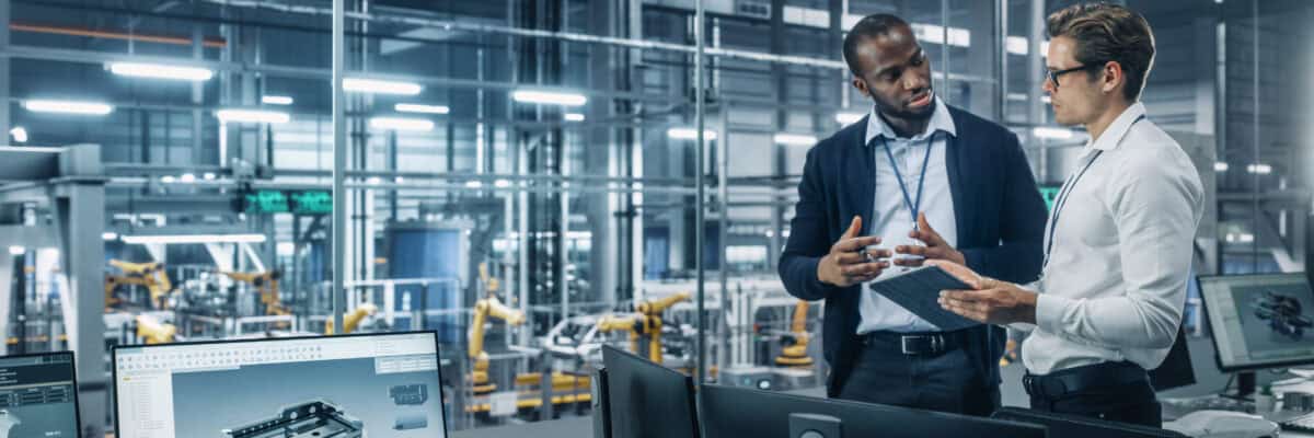 Two Diverse Automotive Industrial Engineers Talking About Vehicle Production while Standing in Office at a Car Assembly Plant. Industrial Specialists Discuss Work Projects on Tablet Computer.